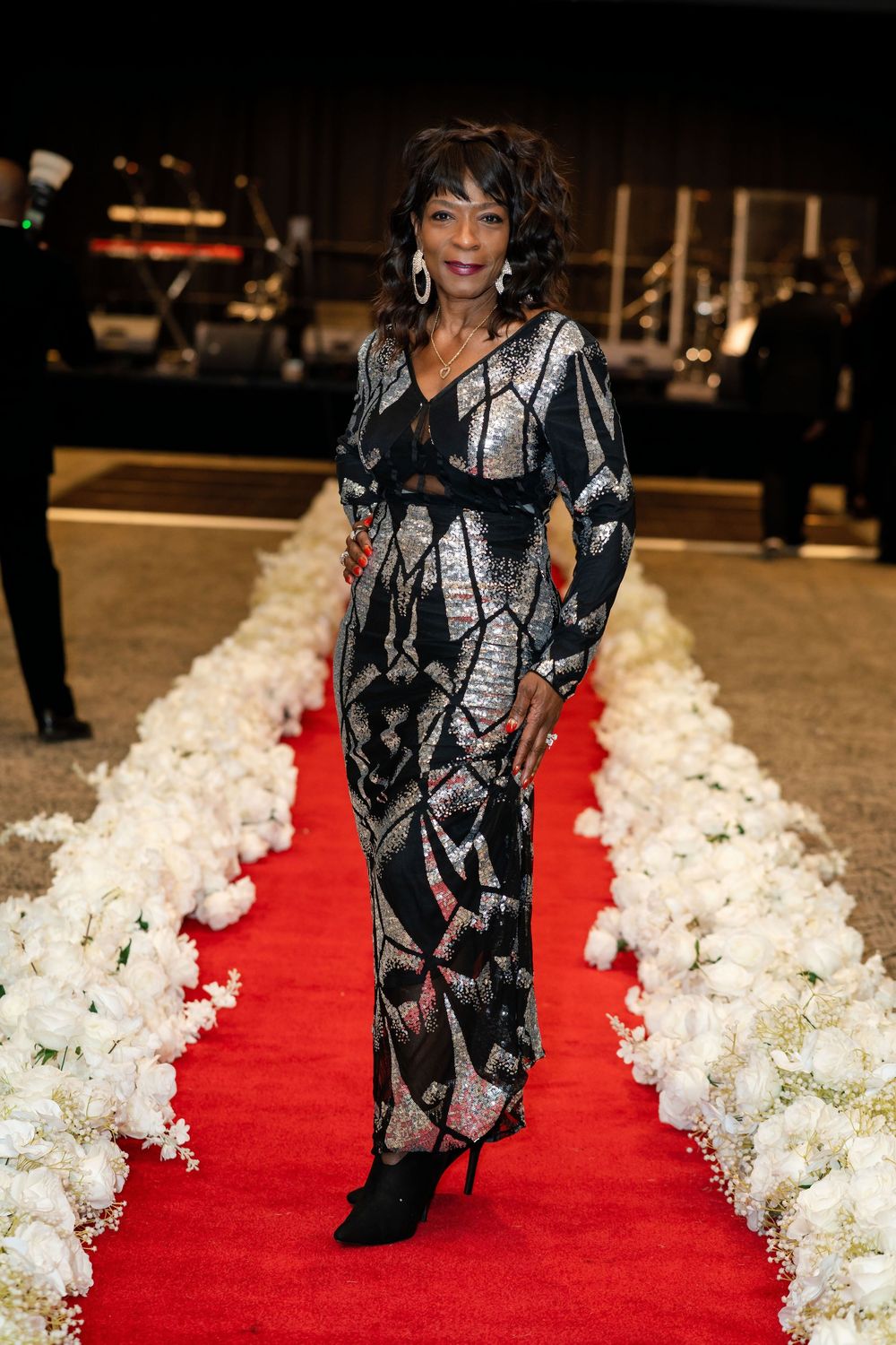 Person walking down a red carpet runway with white floral decorations.