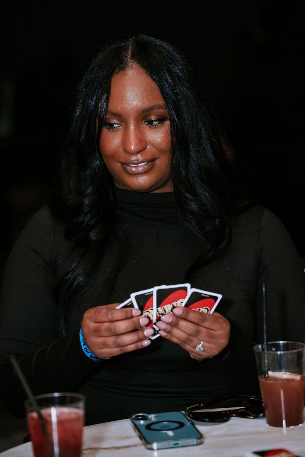 Person playing cards at a table with drinks during an evening event.