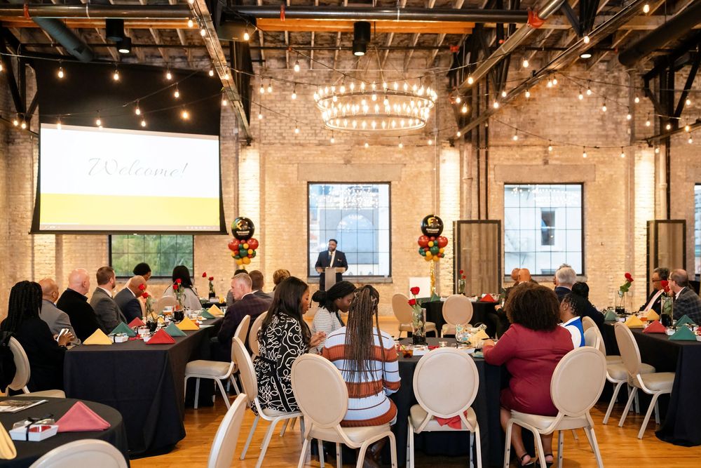 Large industrial event space with exposed brick walls and string lights during a formal gathering.
