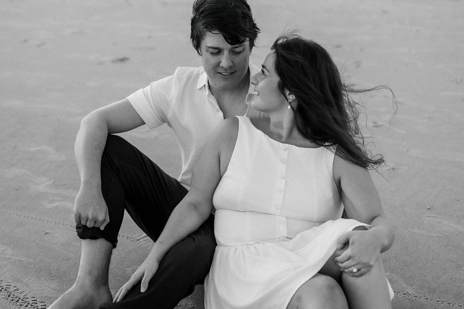 Black and white beach portraits showing tender moments between a couple in casual attire.