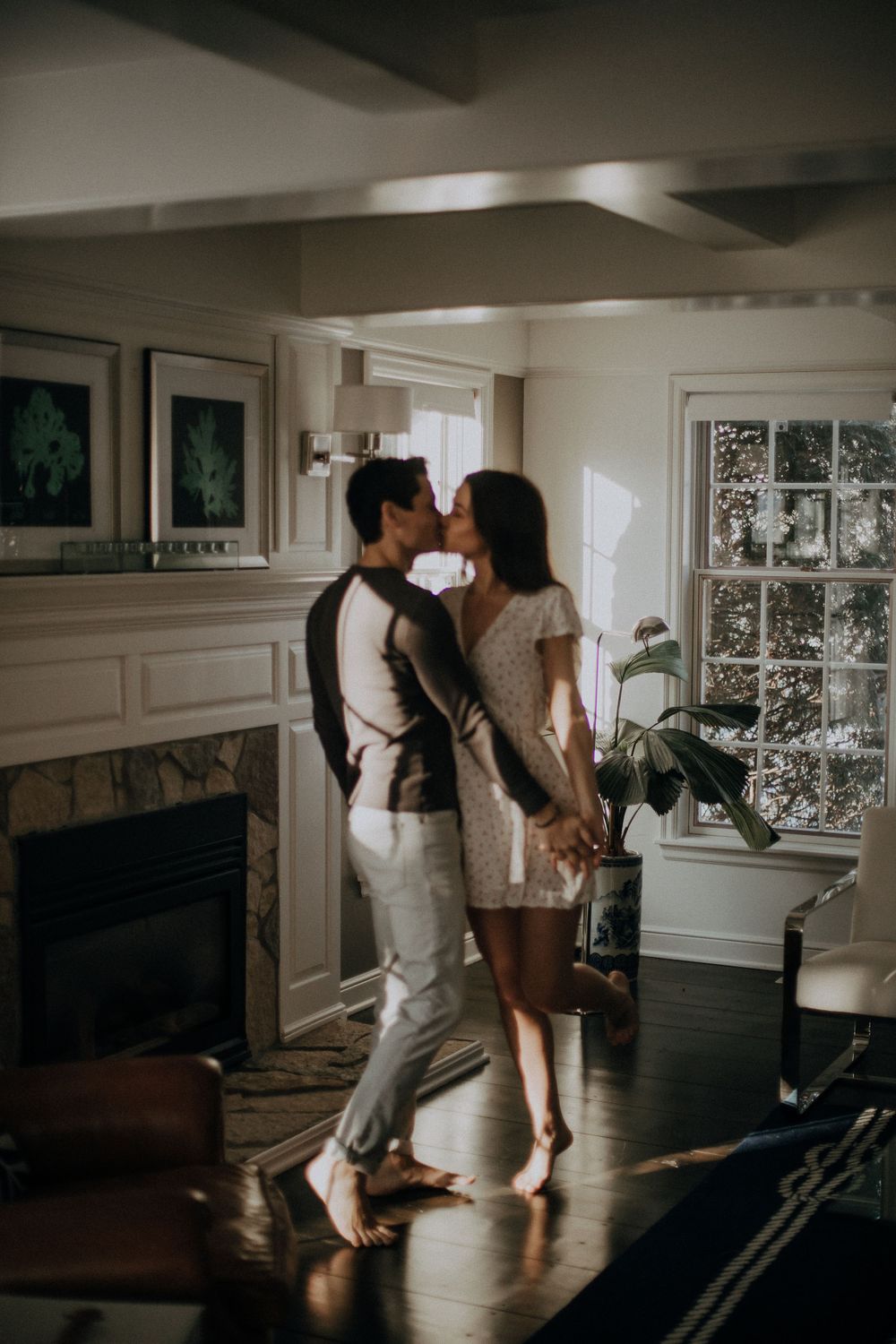 Couple dancing together in sunlit living room with hardwood floors.