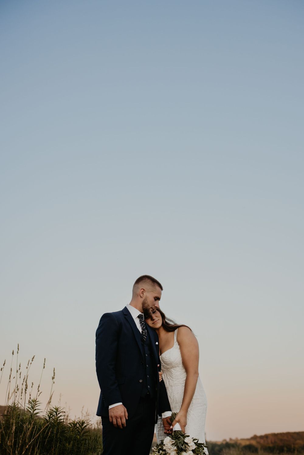 A newlywed couple embraces during golden hour in a field of tall grass.