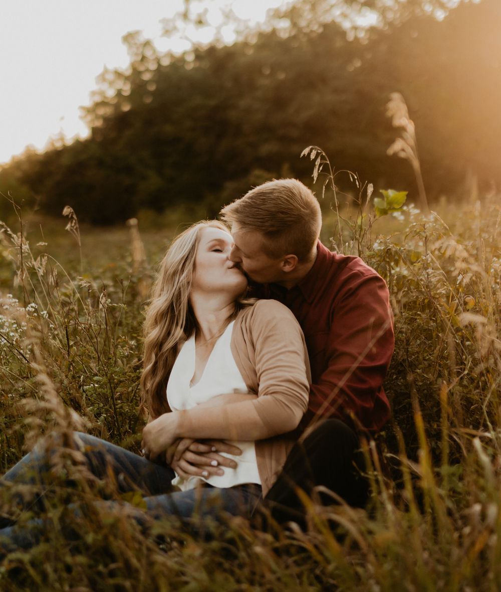 Intimate moment shared between couple in tall grass during golden hour sunset.