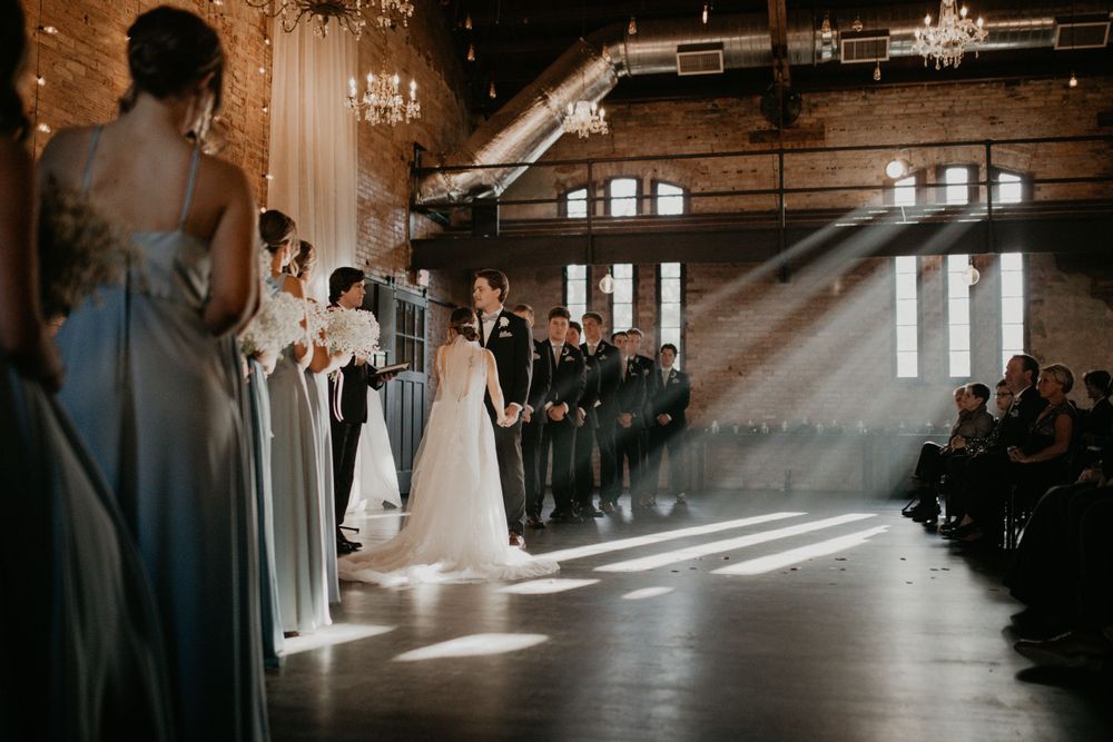 Sunbeams stream through windows during a wedding ceremony in an industrial-style venue.