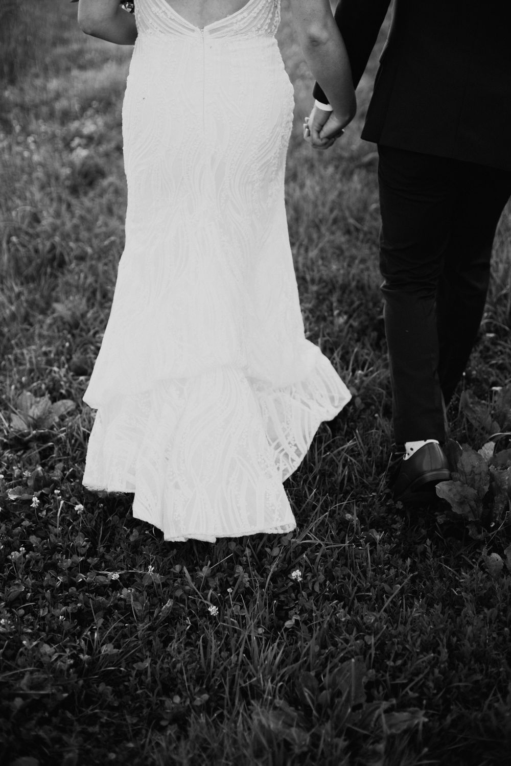 A black and white detail shot of a wedding dress against grass.