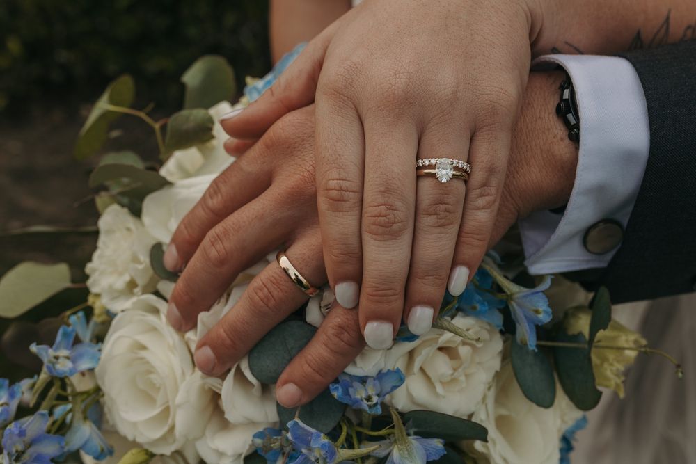Close-up of hands showing wedding rings with white flowers and greenery in the background at San Clemente Shores.