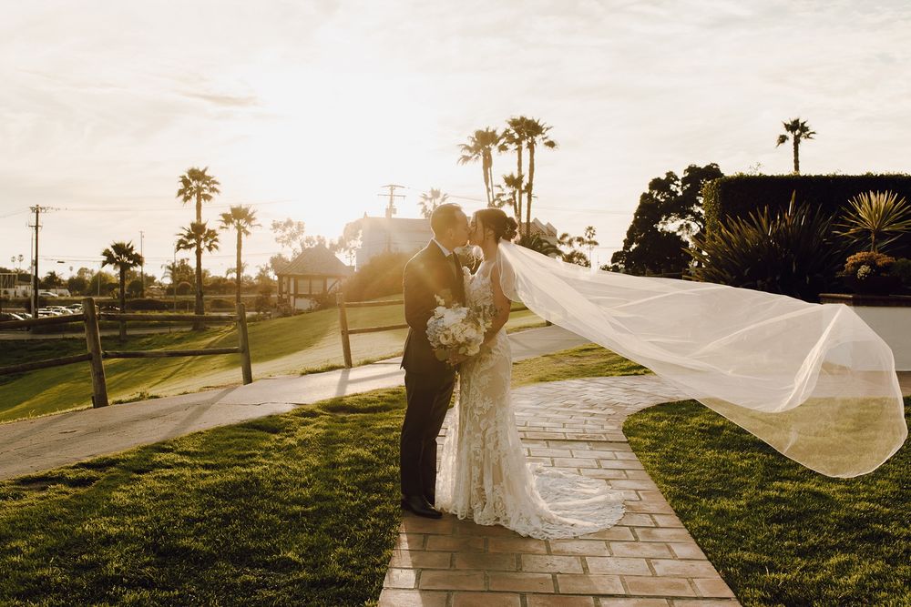 A flowing wedding veil catches the sunlight as it billows in the breeze during an outdoor sunset photoshoot at San Clemente Shores.