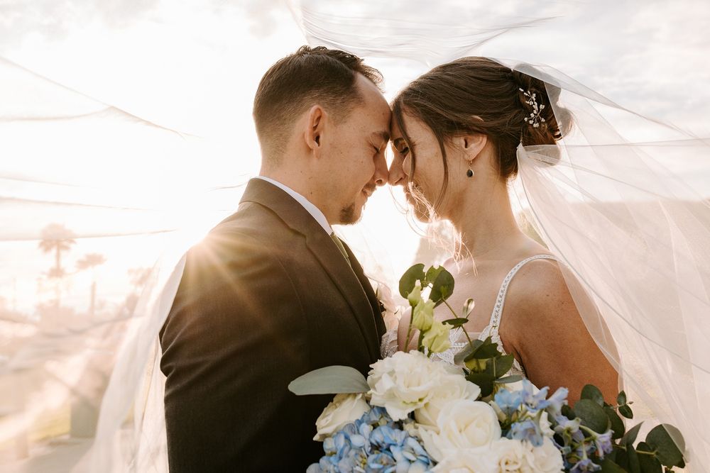 Romantic wedding couple embraces under a flowing white veil during golden hour photography session at San Clemente Shores.