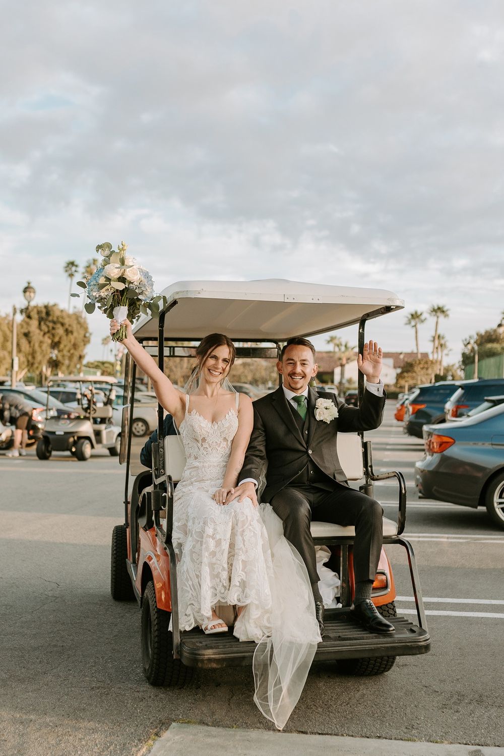 Newlywed couple celebrates riding in a golf cart after a beachy wedding ceremony at sunset at San Clemente Shores.