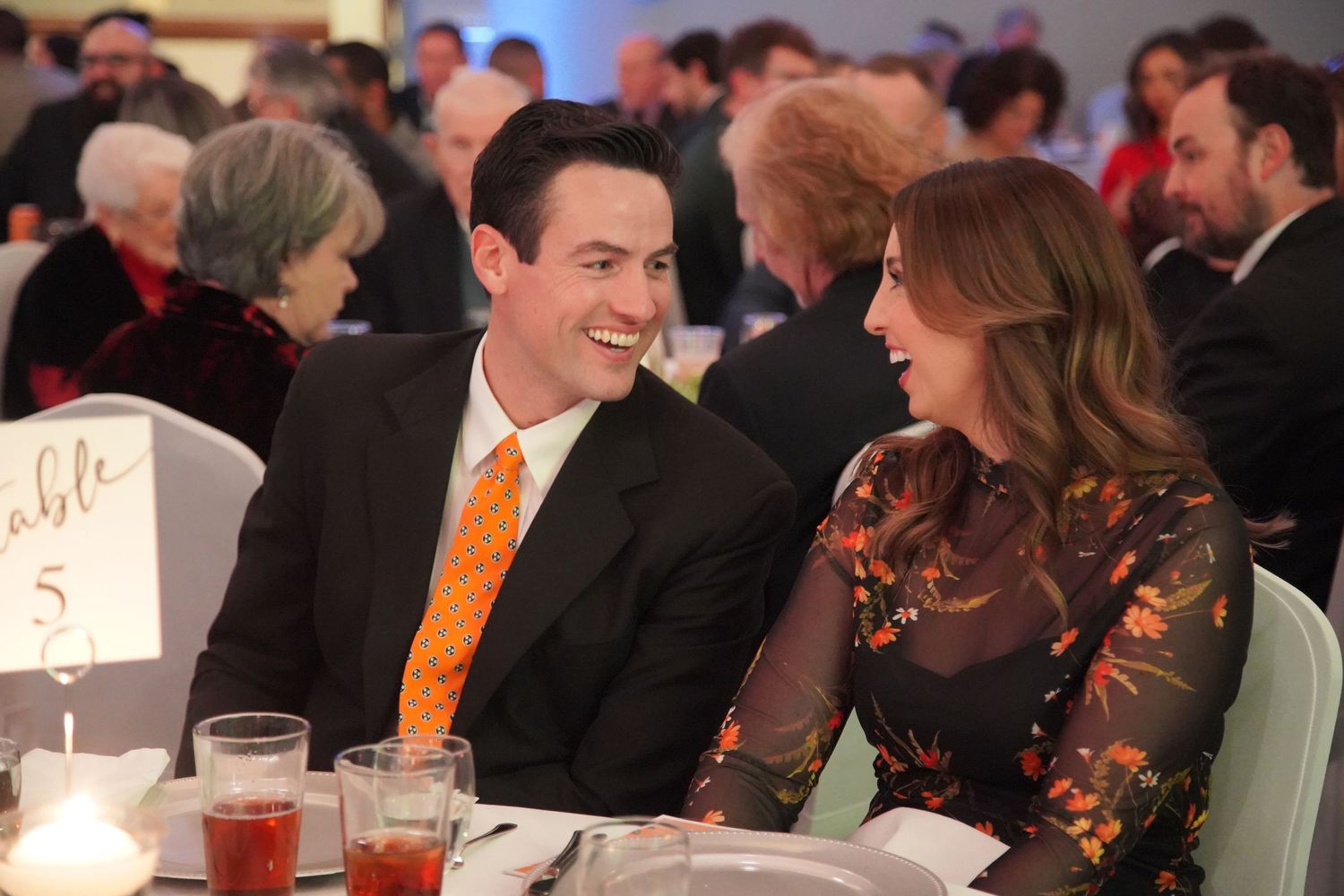 Attendees seated at round tables during a formal dinner event with orange and black decor.