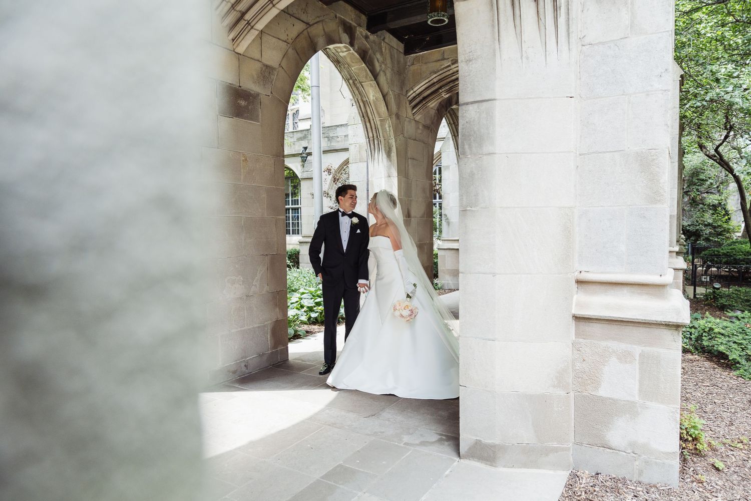 A couple shares a romantic moment under stone archways in a garden setting during their wedding photoshoot.