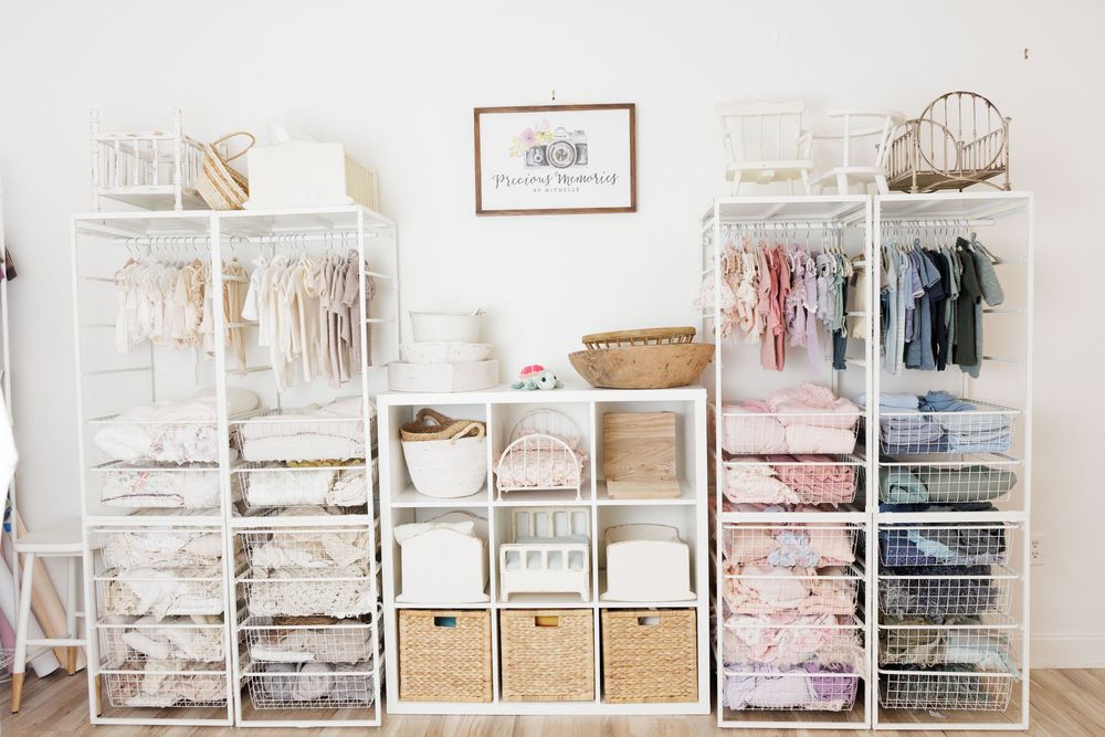 White nursery closet organizer with shelves, baskets, and hanging baby clothes in soft pastel colors.
