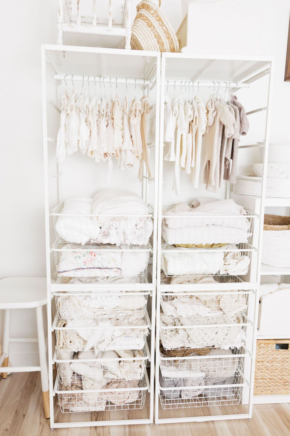 White nursery closet organizer with hanging baby clothes, folded blankets, and wire storage baskets.