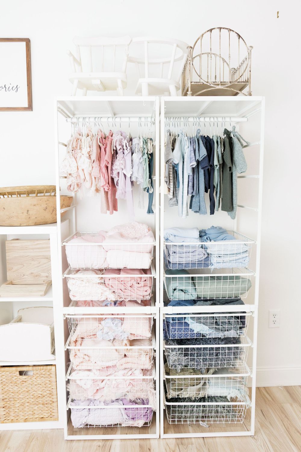 Organized white open closet with pastel baby clothes on hangers and neatly folded items in wire baskets.