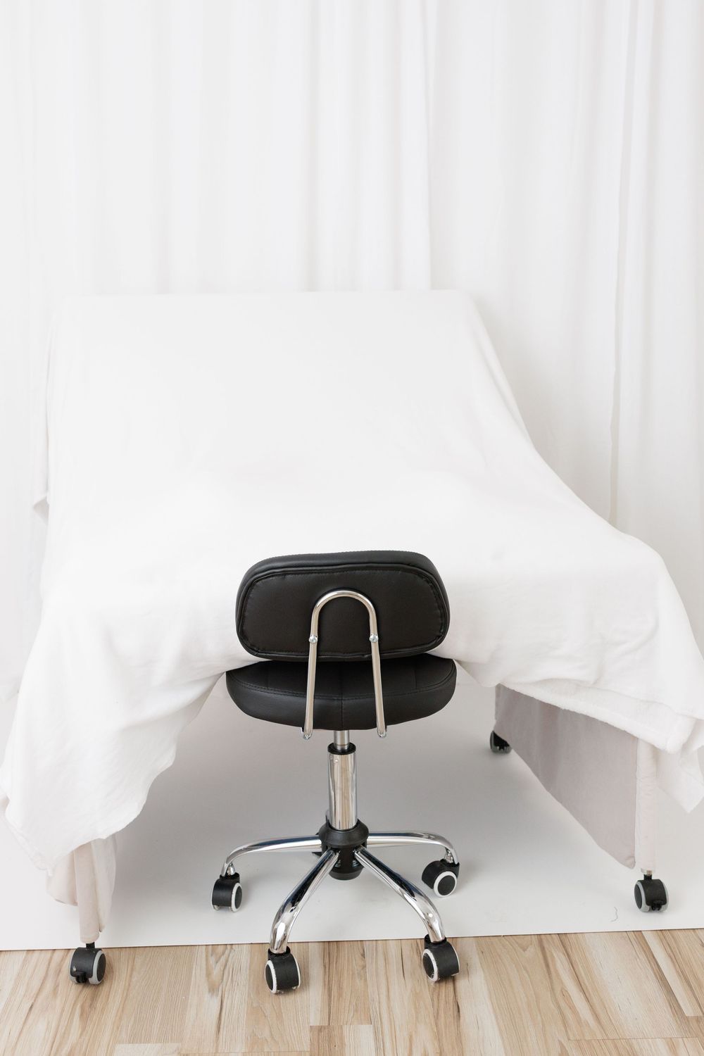 Black leather office chair on wheels in front of a white medical examination table in a clean clinical room.