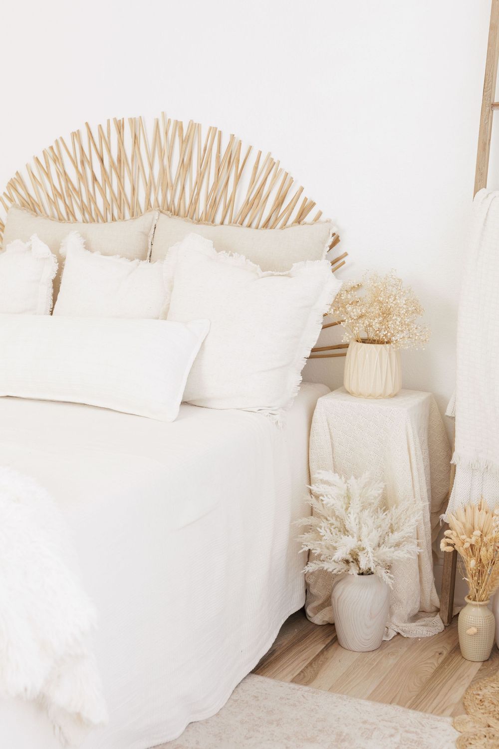 Boho bedroom with rattan sunburst headboard, white bedding, and dried pampas grass in neutral vases on nightstand.