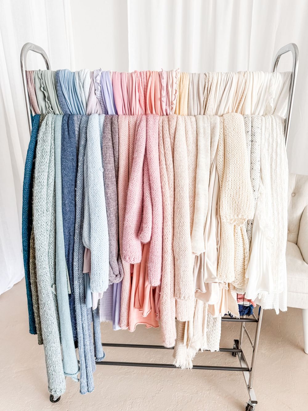 Clothing rack displaying a minimalist wardrobe with soft pastel garments in pink, blue, and white tones.