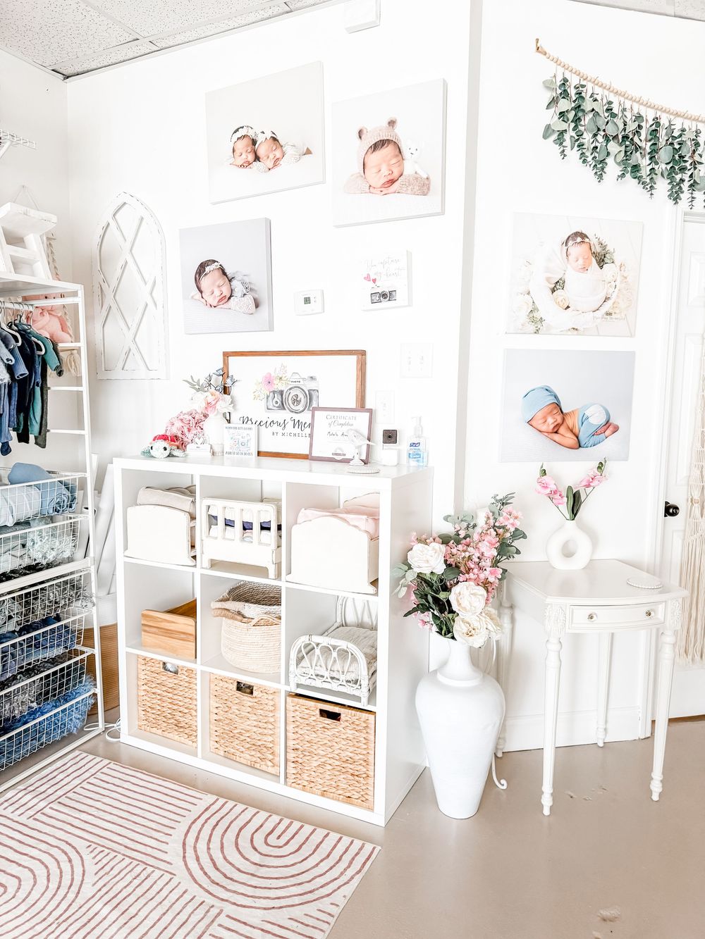 Bright white nursery room with photo gallery wall, cube storage unit, wicker baskets and floral decor accents.