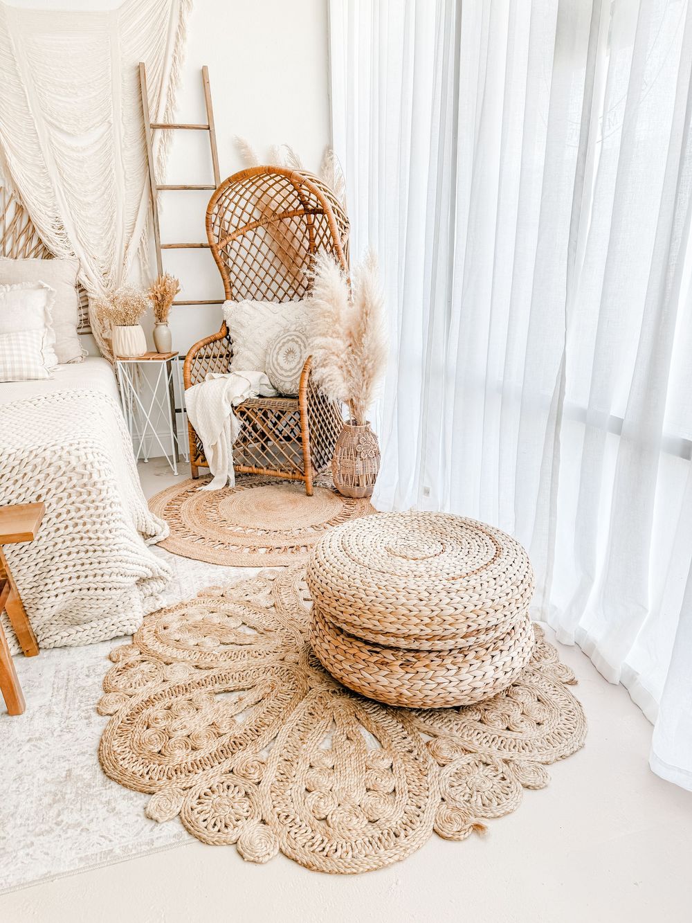 Natural woven rattan floor cushion with decorative pattern displayed against white curtains in a bright interior setting.