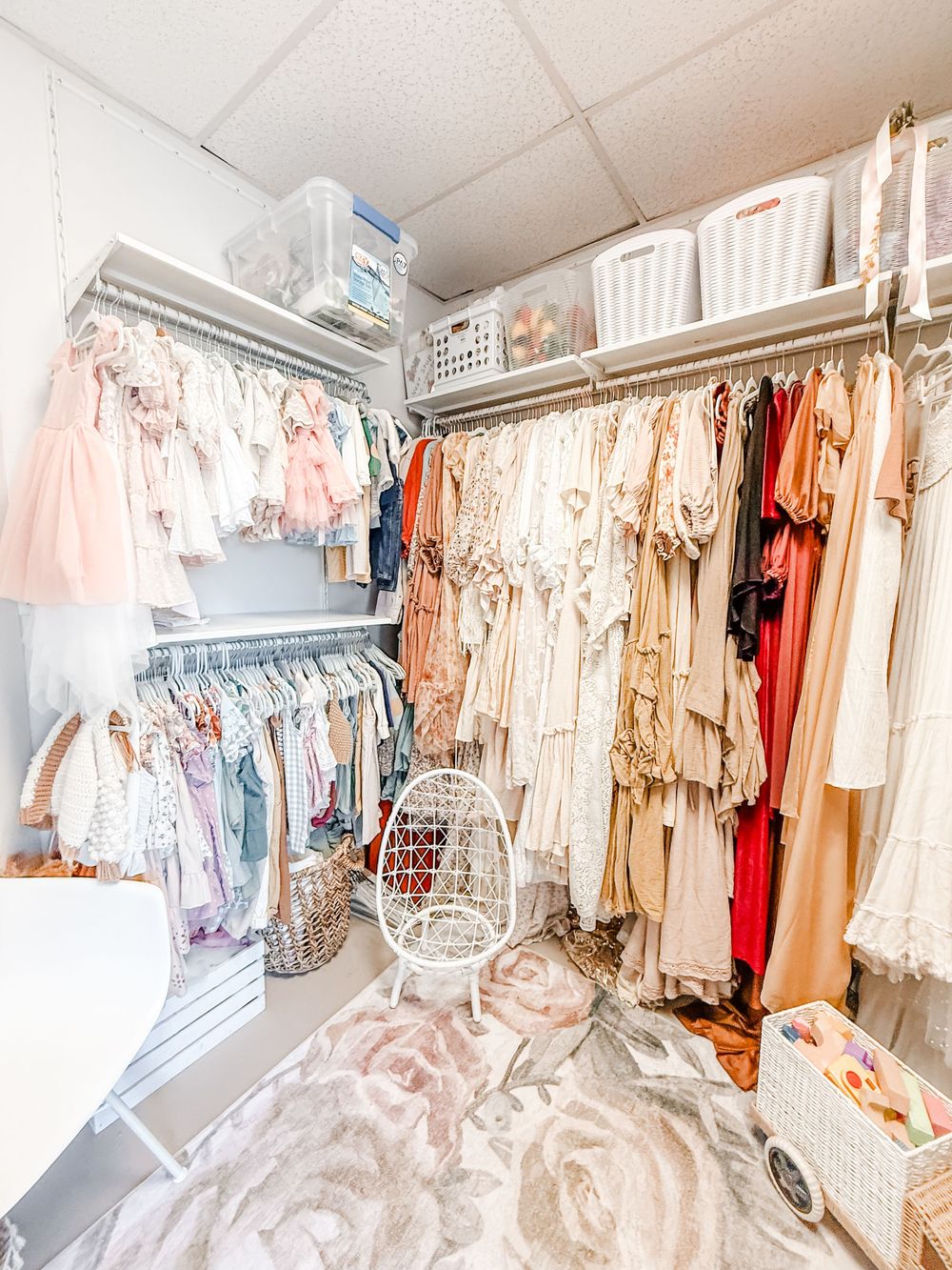 Organized walk-in closet with pink and neutral clothing, featuring white storage baskets and hanging garments in soft tones.