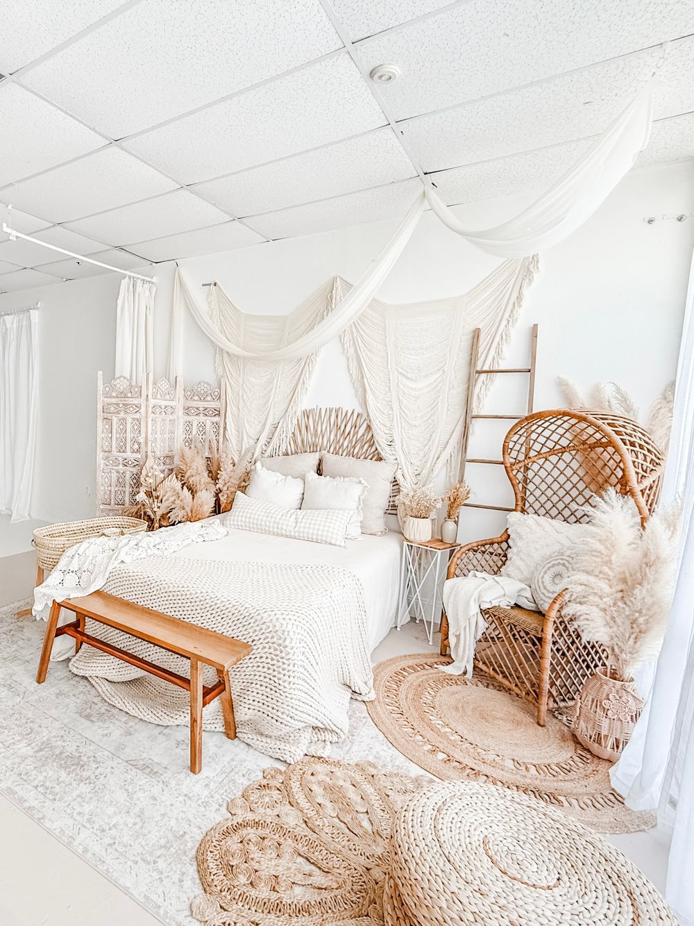 Boho bedroom with white canopy bed, rattan furniture, macrame wall hangings, and circular jute rug in neutral tones.