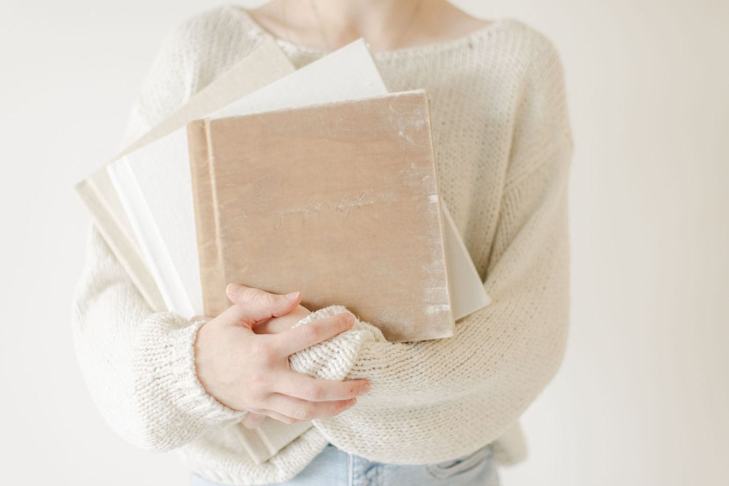 Woman holding three photo albums in a beige sweater.