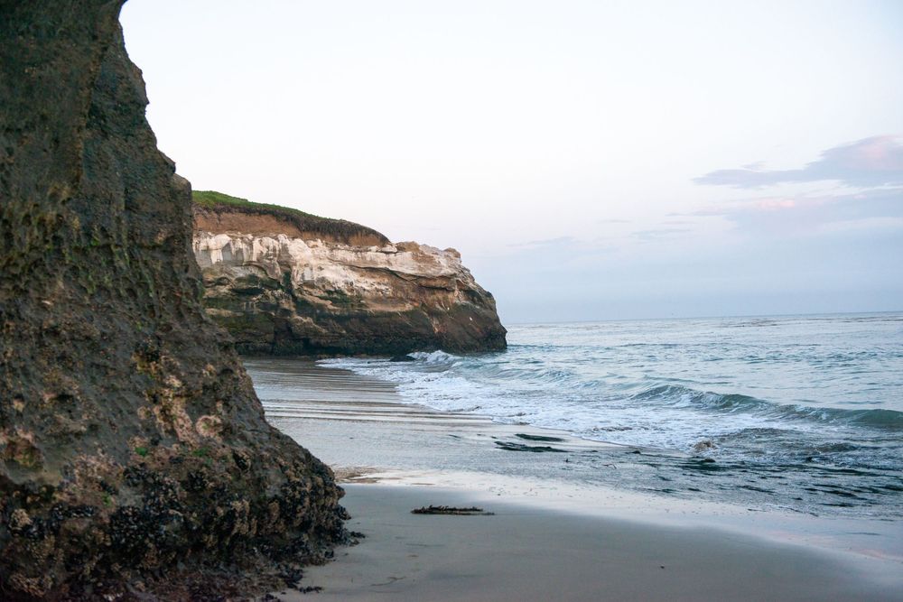 Scenic coastal view with rugged cliffs and ocean waves crashing against rocky shoreline at sunset.
