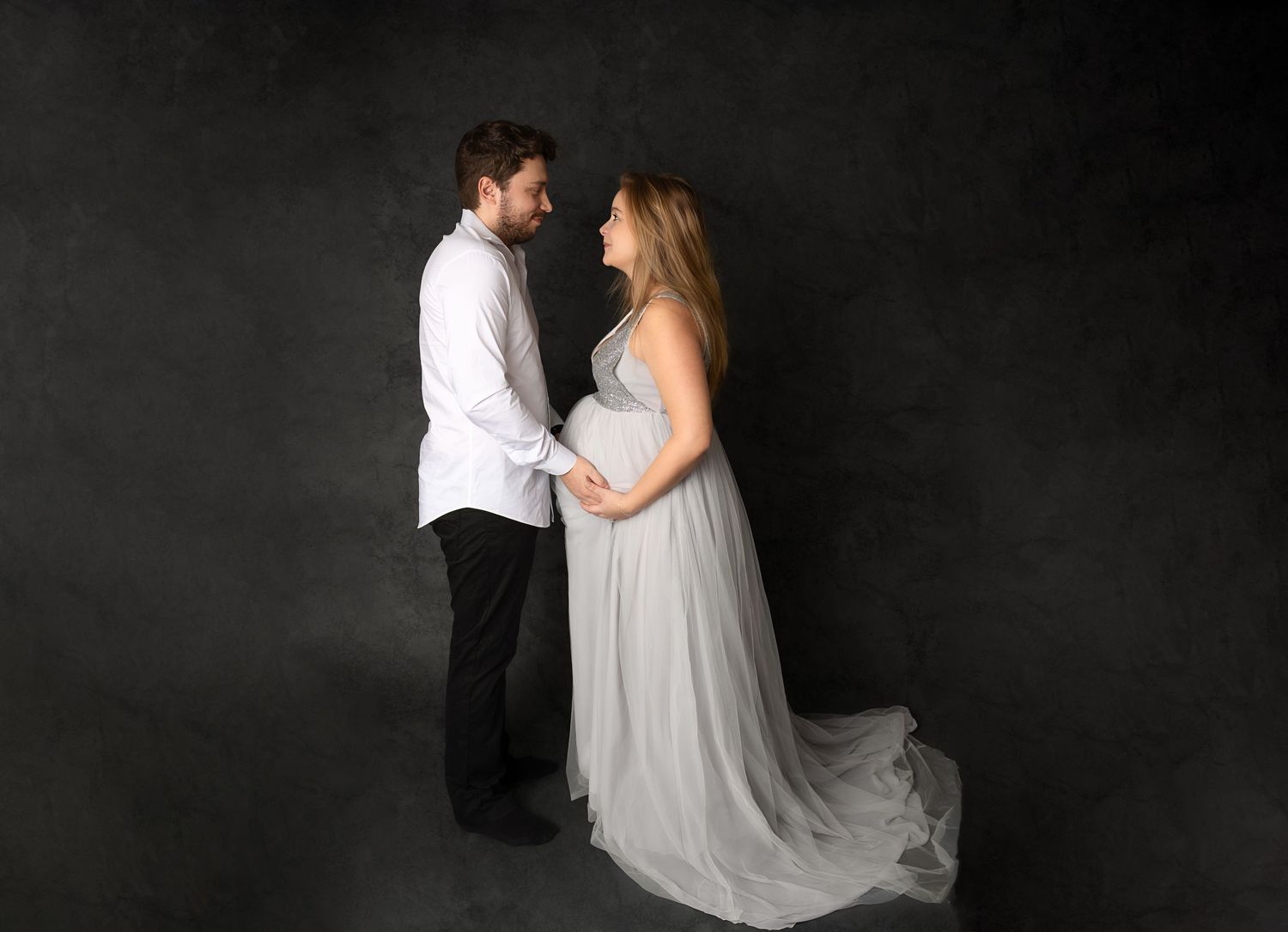 A romantic black, white and grey maternity portrait series showing a couple in intimate poses against a dark backdrop.