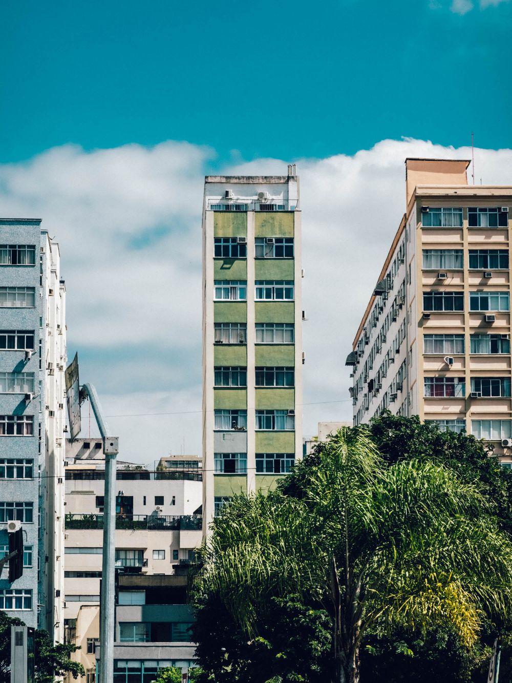 Colorful residential apartment buildings with white and pastel facades against a bright turquoise sky in an urban setting.