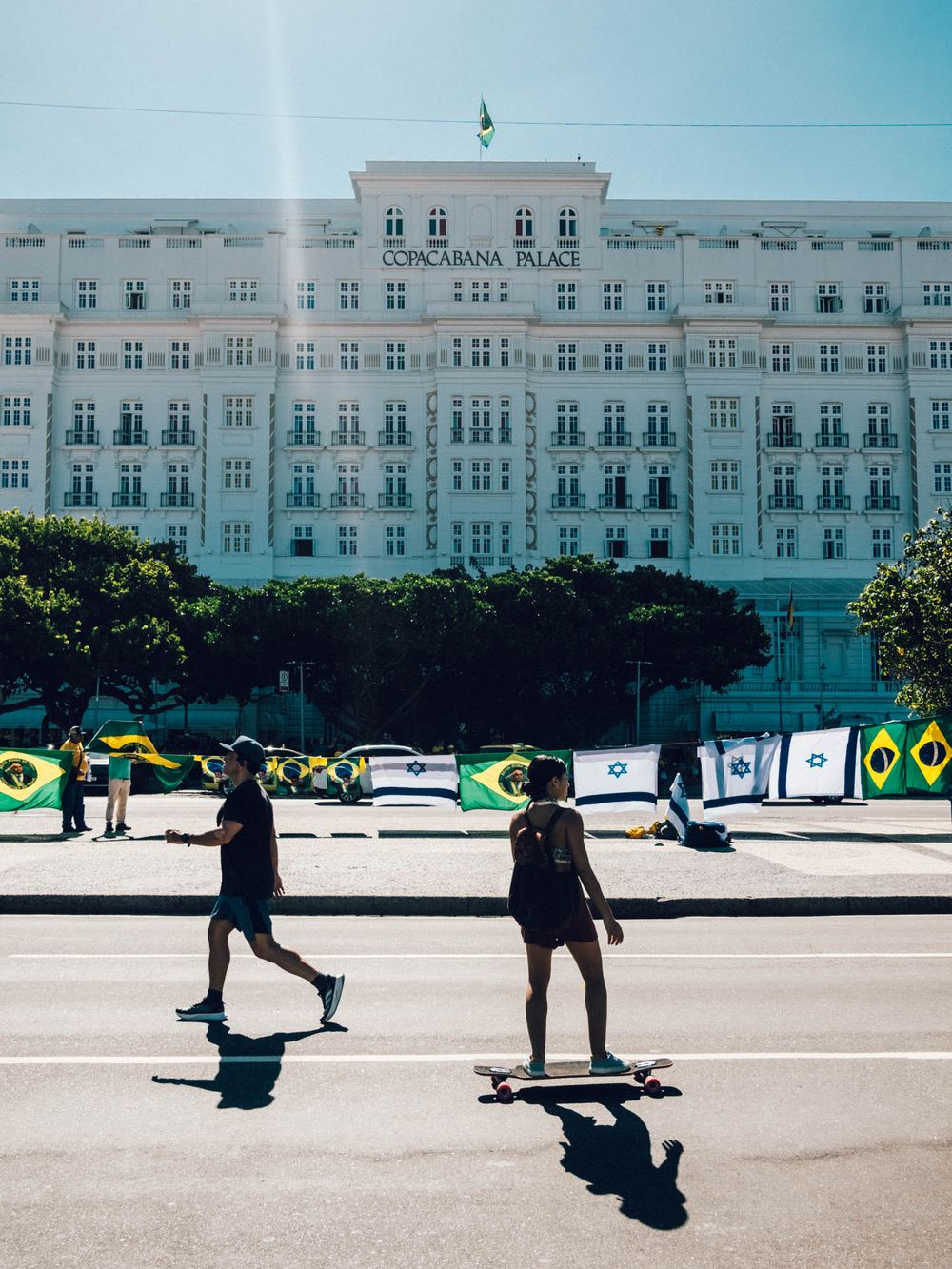 Skateboarders practicing tricks in front of a grand white classical building on a sunny day.