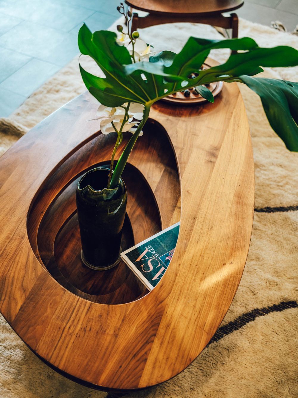 A modern wooden coffee table with a circular cutout planter featuring a green potted plant on a beige carpet.