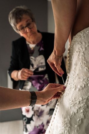 Close-up sequence of hands adjusting and fastening the back of an ornate white lace wedding dress.