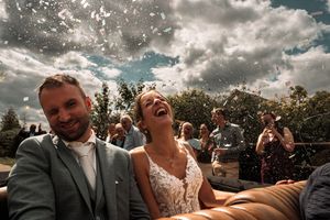 A joyful moment captured at an outdoor wedding ceremony with guests visible in the background under dramatic clouds.