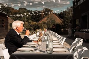 An elegant outdoor dinner table setup with white linens and string lights overhead at a rustic venue.