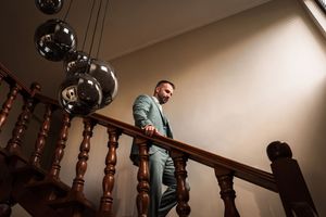A person in a teal jacket walks up a wooden staircase in a dimly lit interior space.