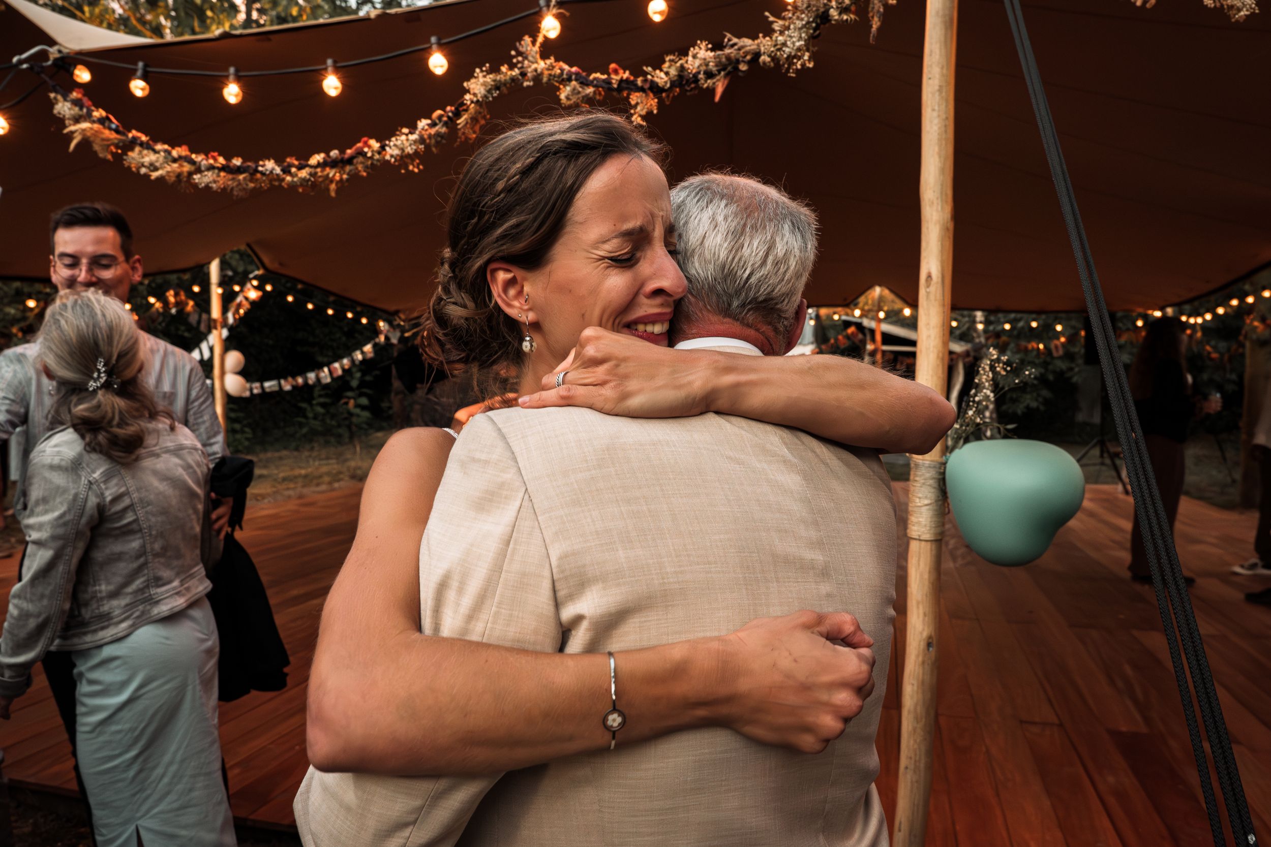Couples dancing and embracing on a wooden dance floor under warm string lights at a celebration event.