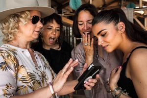 A group reacts with excitement while looking at a mobile phone.