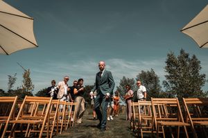 Guests seated in wooden chairs under beige umbrellas at an outdoor wedding ceremony with a scenic mountain backdrop.