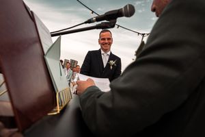 A microphone stands on a table at a formal event with people seated in the background.