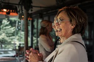 A person wearing glasses laughs joyfully while sitting in what appears to be a vehicle interior.