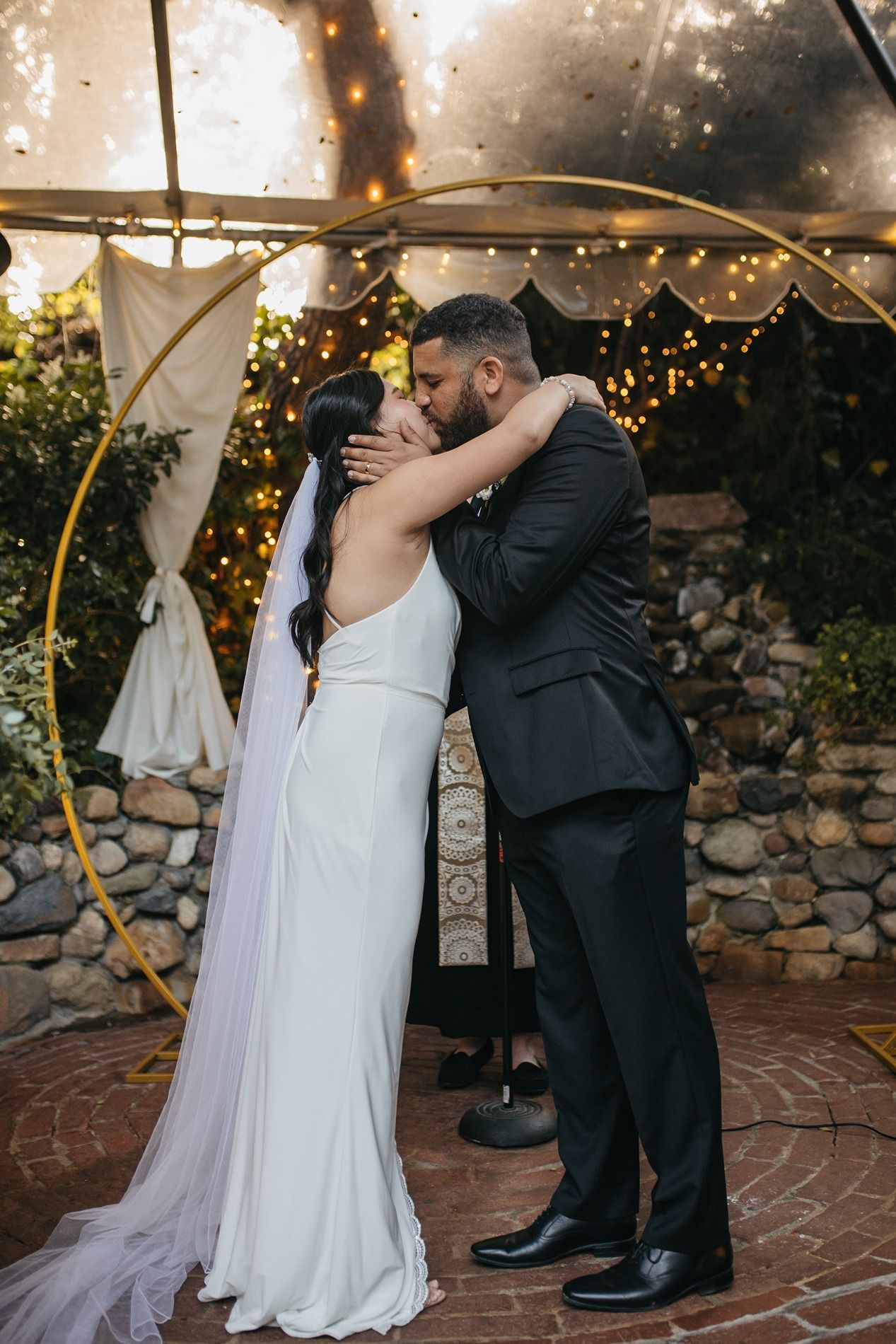 A romantic first kiss at a wedding ceremony under twinkling lights and stone walls Inn of the Seventh Ray in Topanga, California.