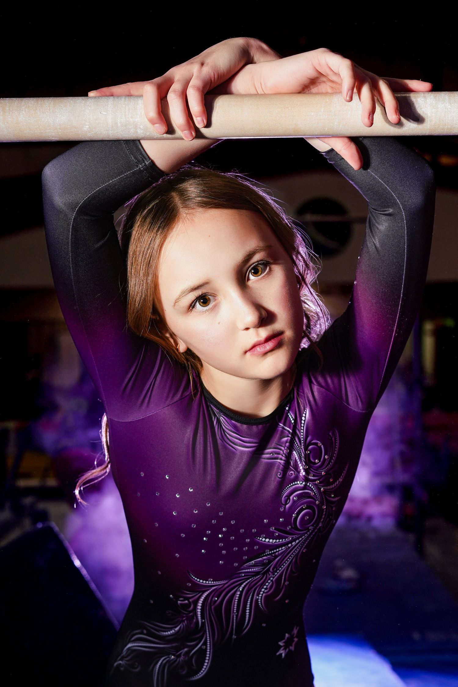 Gymnast in purple leotard performs graceful movements under dramatic lighting in a series of artistic poses.