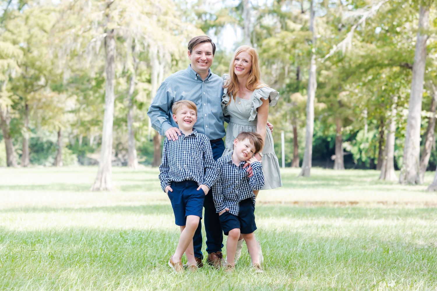 A happy family enjoys a playful moment together outdoors in a sun-dappled park setting.