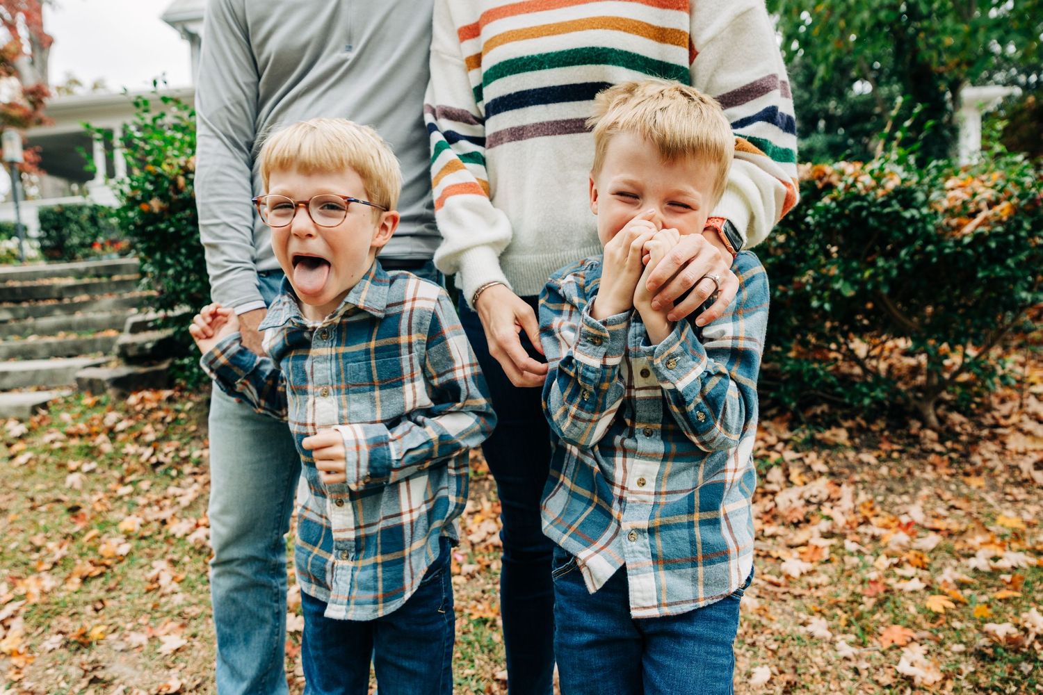 A candid outdoor photo showing playful moments in autumn leaves with plaid shirts and striped sweaters.
