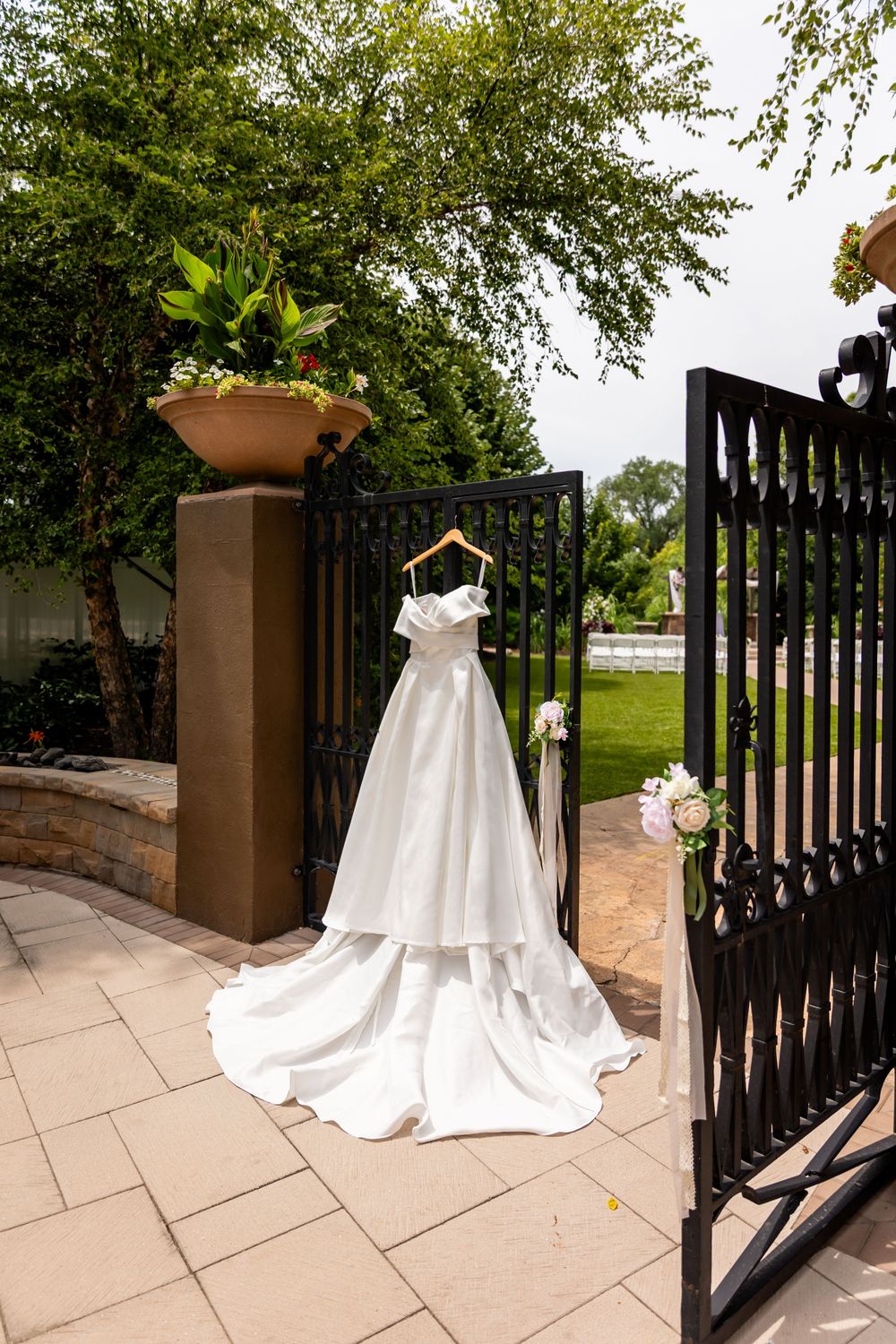 Elegant white wedding dress displayed against black iron gates in garden setting at Villa Aletta in Omaha, NE.