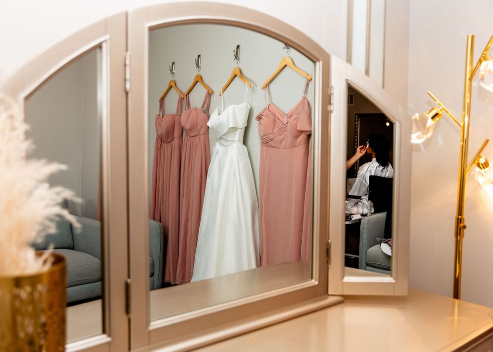 Pink bridesmaid dresses hanging in bridal suite with elegant mirrors and lighting.