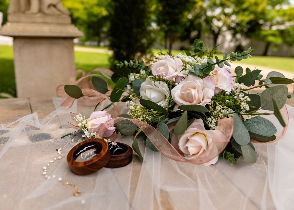 Pink roses and eucalyptus leaves arranged with wedding rings on delicate tulle fabric.