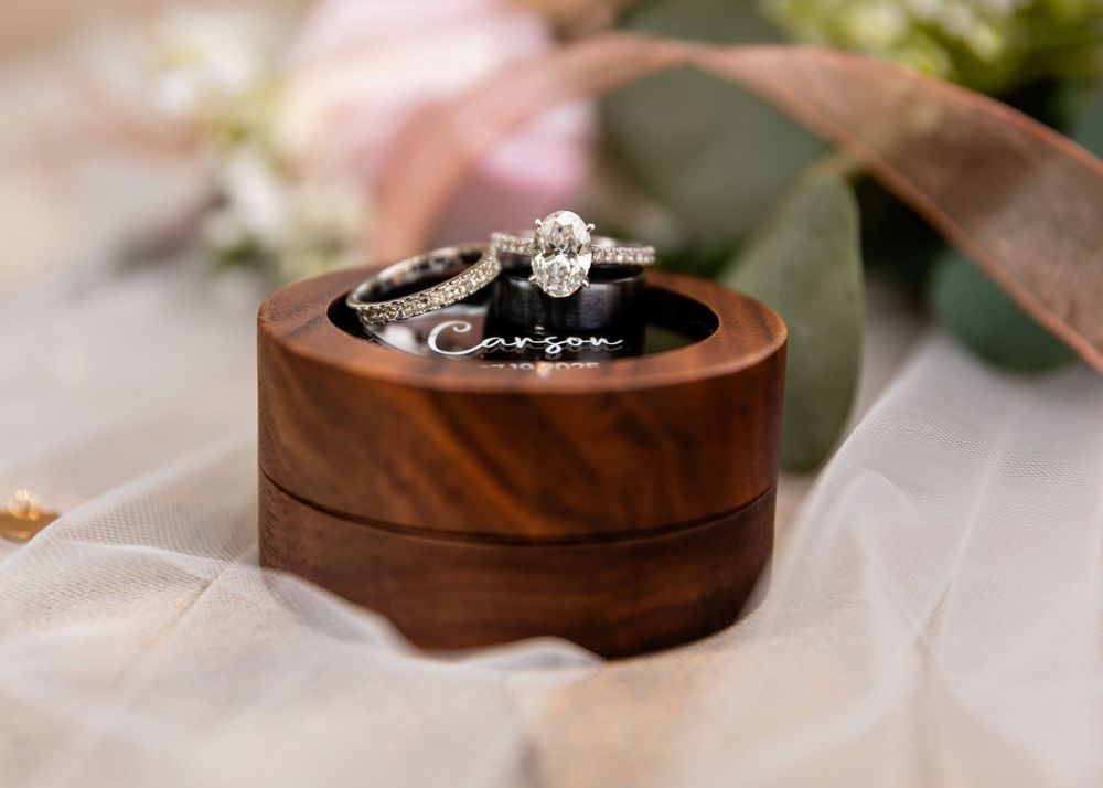 Diamond engagement ring and wedding band displayed in wooden ring box.