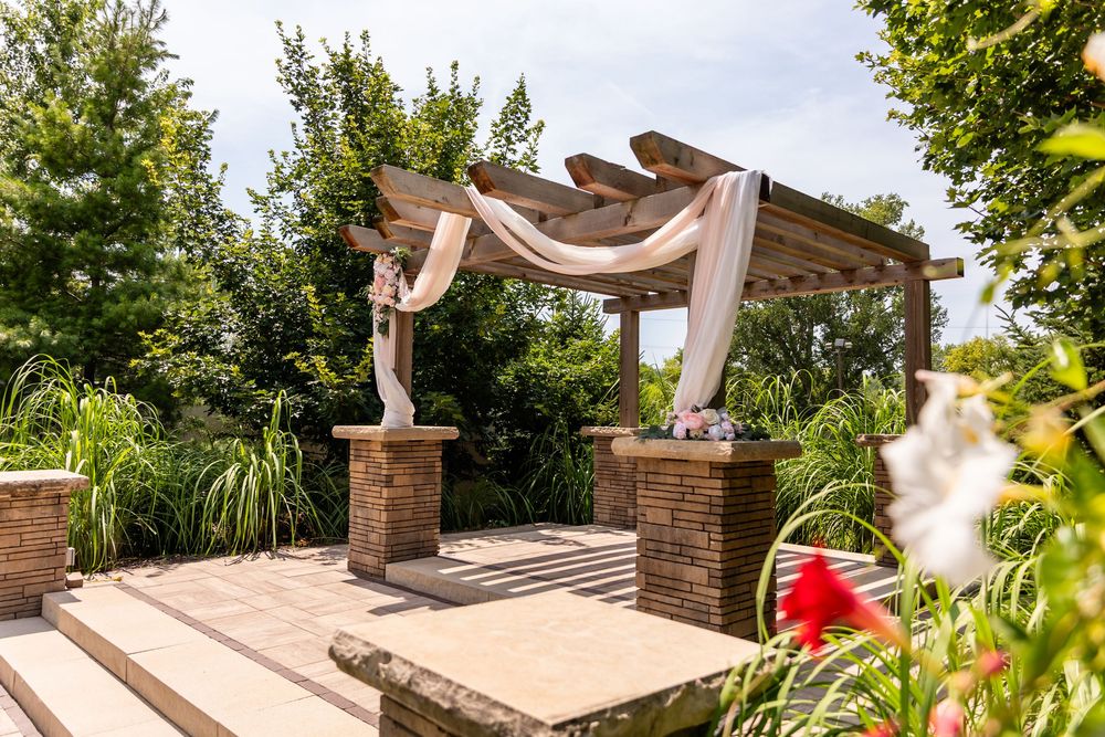 Outdoor wedding ceremony pergola with flowing fabric drapes and stone pillars at Villa Aletta in Omaha, NE.