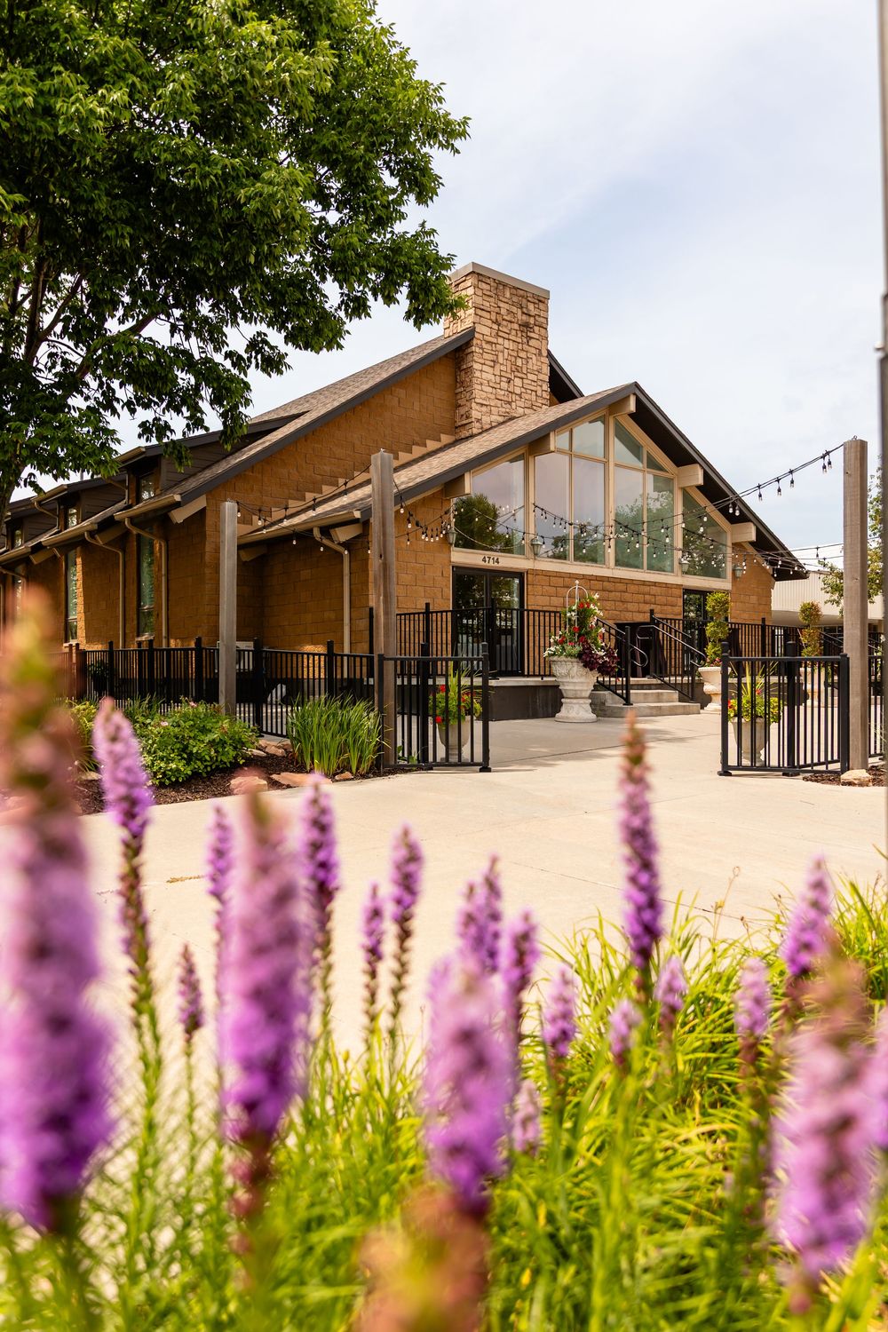 Modern wedding venue exterior with purple flowers in foreground and large glass windows at Villa Aletta in Omaha, NE.